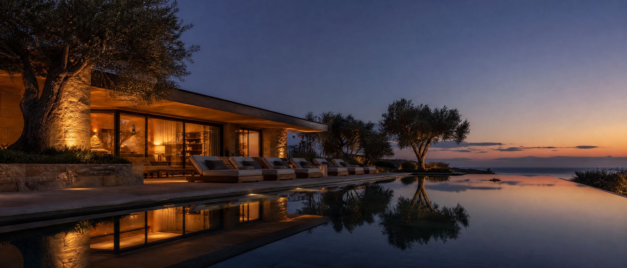 Villa terrace at blue hour with a lit glass pavilion mirrored in a long still pool