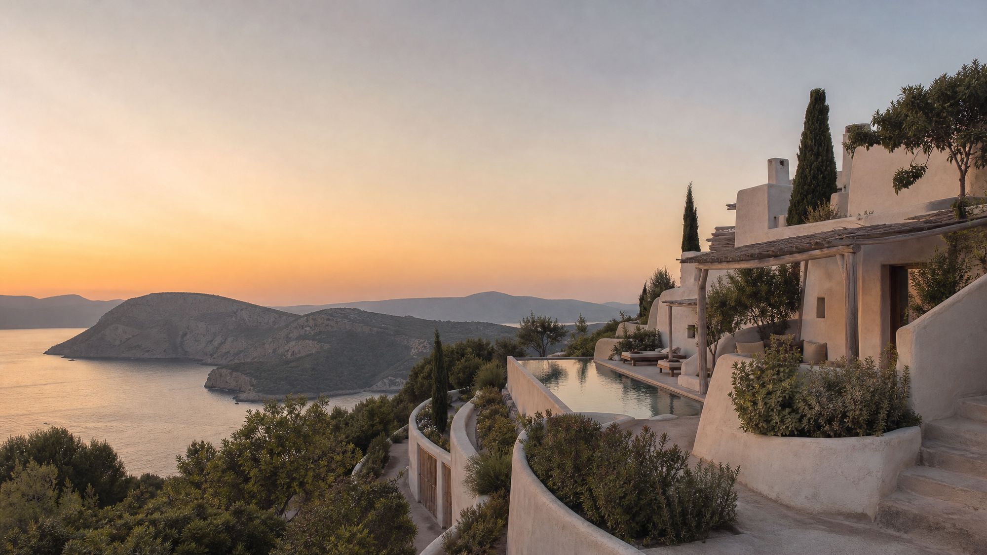 Whitewashed terraced villa with a pool and cypress trees above a bay at sunset, Mallorca